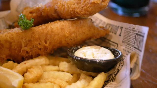 close up view to a plate of fish and chips while using hand pick up french fries from dish for dinner lunch meal