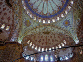 Fototapeta na wymiar Opulent murals and ceiling wall paintings inside Arabic mosque with columns, domes, high walls and lots of windows for daylight impressive interior design and construction architecture from 1001 night