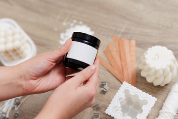 Woman hand holding handmade soy candle jar with white label with space for text