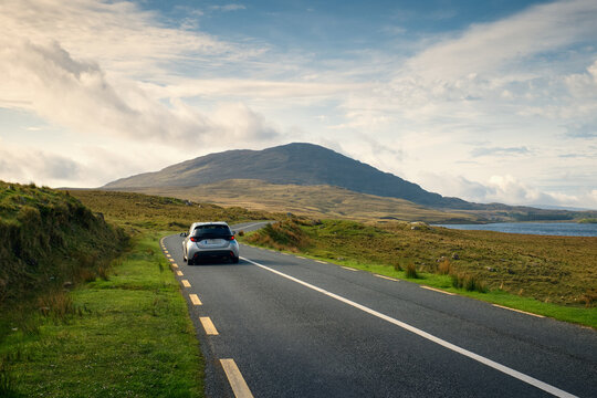 Car driving on empty scenic road trough nature by the lough inagh with mountains in the background at Connemara National park in county Galway, Ireland 