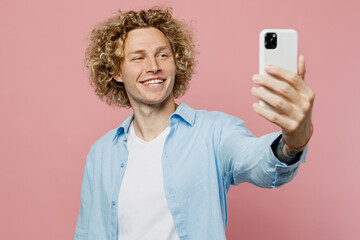 Young fun blond man wear blue shirt white t-shirt doing selfie shot on mobile cell phone post photo on social network isolated on plain pastel light pink background studio portrait. Lifestyle concept.