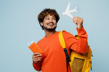 Traveler young teen boy student man wear casual clothes backpack bag hold passport ticket mock up of plane isolated on plain blue background. Tourist travel abroad to study. Air flight trip concept.