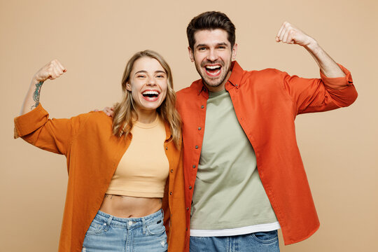 Young couple two friends family man woman wear casual clothes showing biceps muscles on hand demonstrate strength power together isolated on pastel plain light beige color background studio portrait