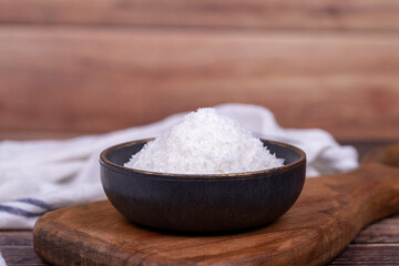 Coconut powder. Grounded coconut flakes on wood floor. Dark bowl of dessicated coconut