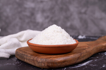 Coconut powder. Grounded coconut flakes on dark background. Earthen bowl of dessicated coconut