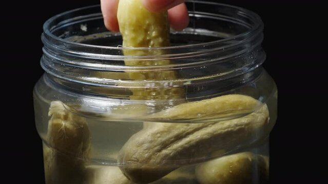 A jar of pickles rotates on a black background and I take out one cucumber.