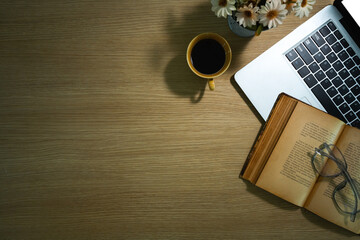 Top view of laptop, coffee cup, old book and eyeglasses on rustic wooden table. Copy space for text