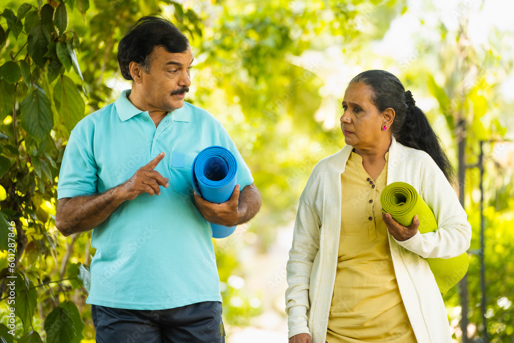 Wall mural Active Indian senior couple with yoga mat by talking each other coming for exercising at park - concept of retirement lifestyle, relationship and communication