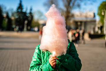 Cotton candy in the hand of a child in a summer park. Sweet food and sugar.