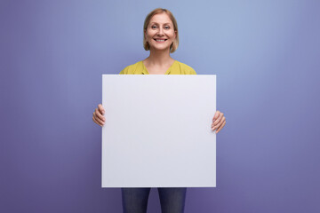 joyful blond mature woman holding paper poster with mocup