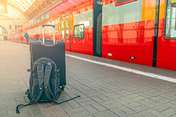 A suitcase and backpack stand on the platform of the railway station in the rays of the rising sun. Travel concept.
