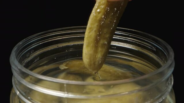 I take out a pickle from a jar on a black background.