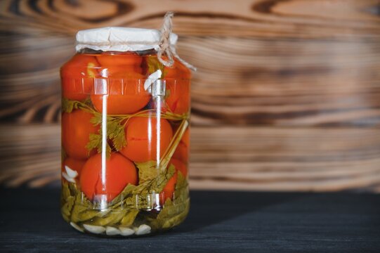 Canned cucumbers and tomatoes with craft lids on a wooden background. Cucumbers and tomatoes with place for text. Stocks of canned food. Harvest, stocks for the winter.