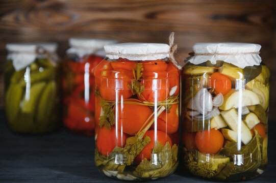 Canned cucumbers and tomatoes with craft lids on a wooden background. Cucumbers and tomatoes with place for text. Stocks of canned food. Harvest, stocks for the winter.