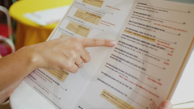 Close-up of beautiful girl hands looking at the restaurant menu, choosing breakfast, meal.