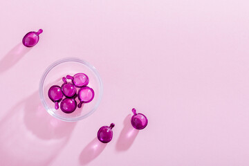 Vitamin capsules in pink, purple color, closeup on pink background, top view