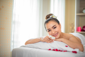 Obraz na płótnie Canvas Beautiful asian woman lying on bed sprinkle with roses in spa room while looking to the camera with smile.