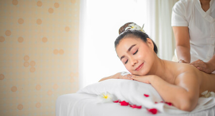 Obraz na płótnie Canvas The skilled hands of the professional masseuse glided over the back of the beautiful asian woman providing a soothing and relaxing massage experience on the bed adorned with scattered roses.