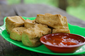 Fried tofu placed on a green plate and complete with chili sauce