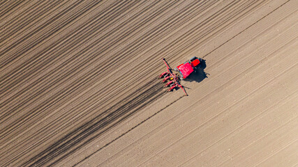 Obraz premium Aerial top view of tractor as dragging a sowing machine over agricultural field, farmland