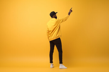 Fototapeta na wymiar Back View Of African American Man Pointing Finger Up Pushing Invisible Button Or Touchscreen Standing Over Yellow Studio Background, Look Upward, Full Length Shot