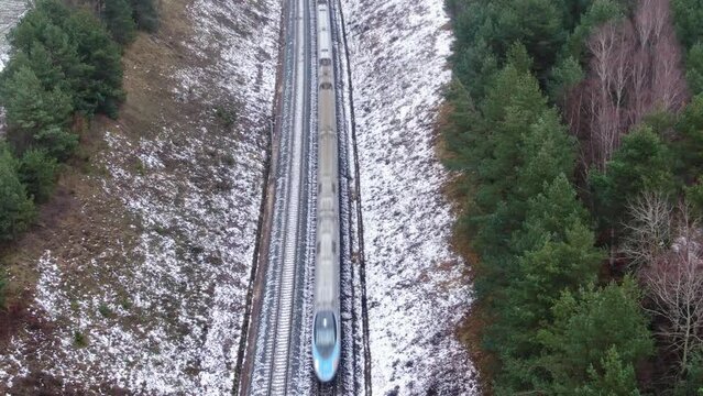 Aerial top down view on high speed express train passing forest on winter day