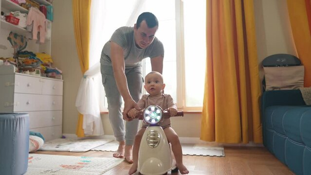 baby rides a motor scooter indoors. dad rides his son teaches him to ride a scooter around the room at home. happy family kid dream concept. parent play baby lifestyle rides a scooter plays indoors