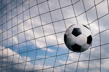 Symbolic of success and victory. classic soccer ball football have black and white color going into in-goal net after shooted in the game with a blue sky background. success concept.