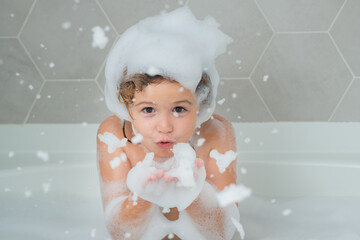 Child blow shampoo foam and bubbles on hair taking bath. Portrait of smiling kid, hair care and...