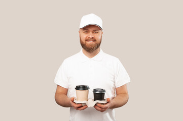 Wide smiling delivery man or barista wearing white uniform is holding two take away cups of coffee.