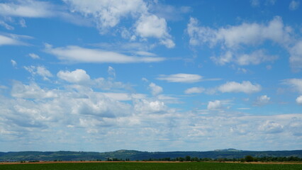 Serene blue sky with fluffy white clouds above crops field and hills in Transylvania, Romania on beautiful summer day