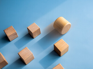 Obraz premium Leadership, business success, unique, difference, challenge, and motivation concepts. Wooden cylinder block rolling faster, leading first and following with wood cube blocks on blue background.
