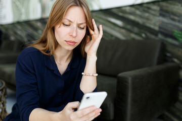 Young woman sad,reading bad news email, break up message from ex-boyfriend on smartphone sitting lonely on couch in living room. Depressed unhappy female desperate of heartbreak sms on mobile phone