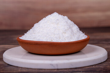Grounded coconut flakes on wooden background. Coconut shavings in clay bowl. Close up