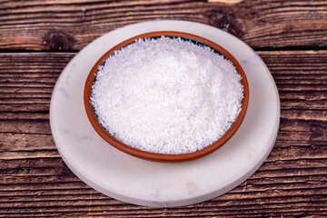 Grounded coconut flakes on wooden background. Coconut shavings in clay bowl