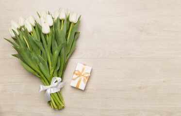 White tulip bouquet and gift box on wooden background, top view