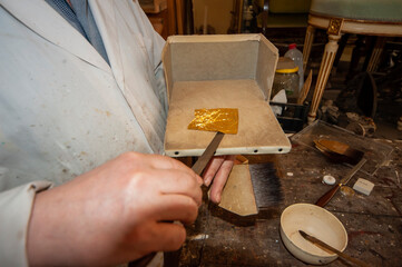 Fototapeta na wymiar Artigianato, artigiano. Doratore al lavoro con foglia d'oro per restauro doratura.