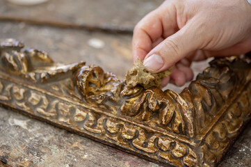 Artigianato, artigiano. Restauro di cornice dorata d'antiquariato, mani in primo piano al lavoro.