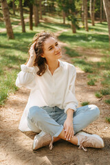 Obraz premium Peaceful curly woman has a moment of relax enjoying sitting in a forest. Vertical shot.