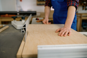 Closeup of carpenter cutting wooden board on circular saw workbench