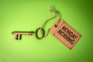 Monday Morning Concept. Golden key with cardboard price tag on green background