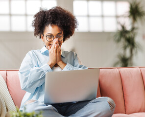 beautiful young smiling ethnic woman smiling and rejoices in victory   sitting on sofa and working...