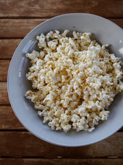 popcorn in a blue bowl on a wooden table in the background. top view
