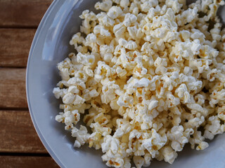 close-up of popcorn in a blue bowl on a wooden table in the background. top view