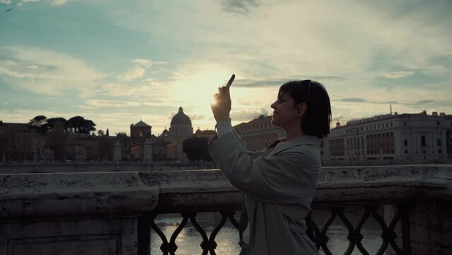 Beautiful young female in Rome Italy taking photos with phone on sunset enjoying her vacation