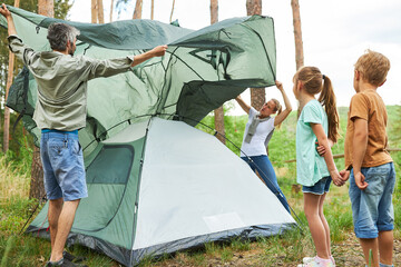 Parents with two kids setting up tent for camping in nature