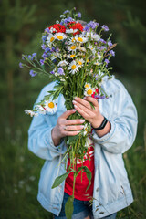the girl covers her face with a large bouquet of wildflowers
