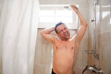 an ordinary man takes a shower and washes his hair in a small bathroom with a shower head on the...