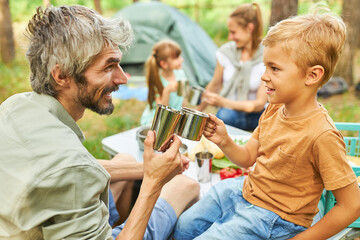 Father and son toasting mugs while camping in forest