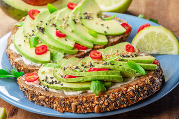 Avocado toast - bread with avocado slices, pieces chilli pepper and black sesame on blue plate closeup.